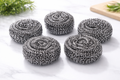 Five silver stainless steel brush balls on white marble surface, crafted with tightly coiled wire.